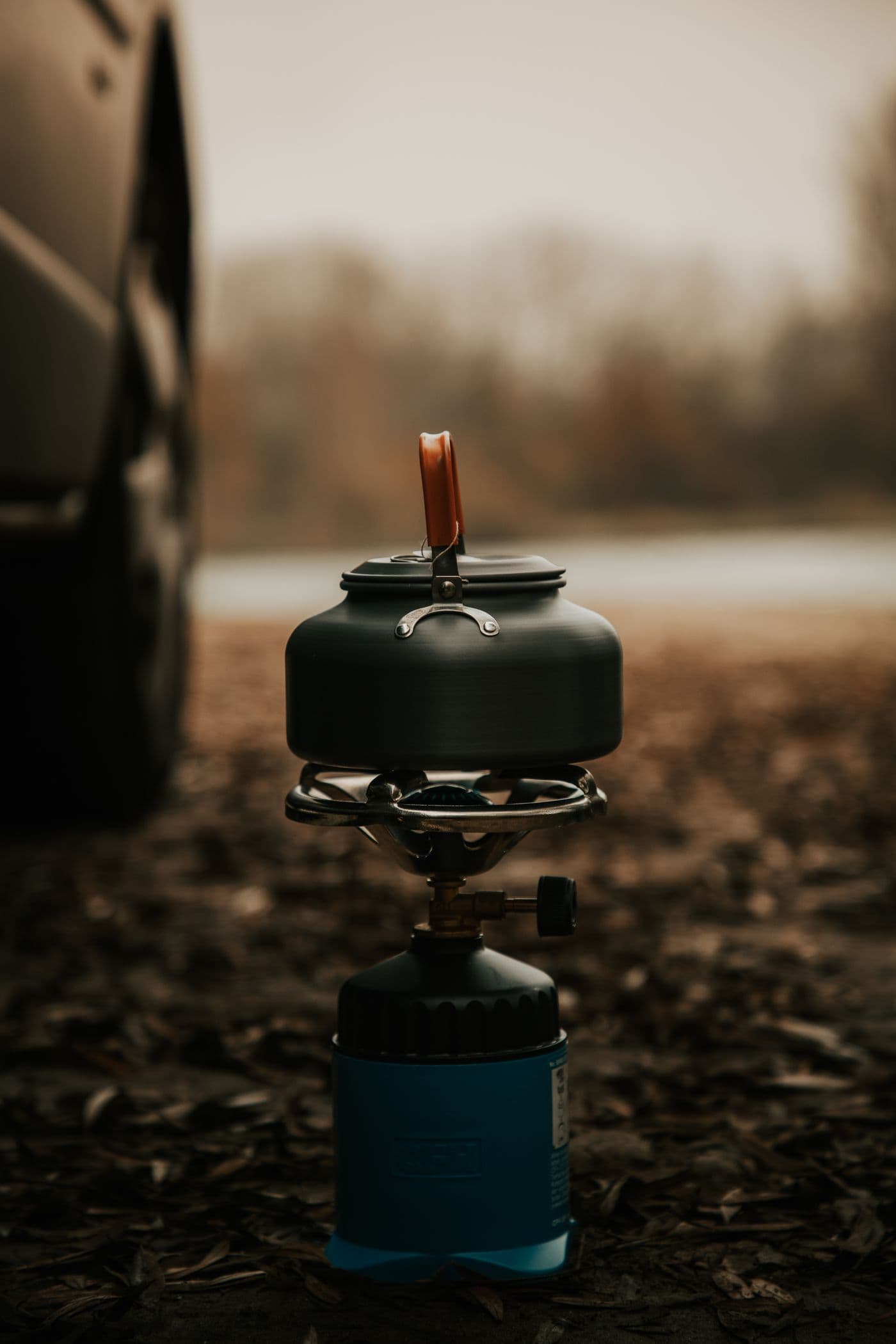 A camp stove and cooking pot set among fallen leaves